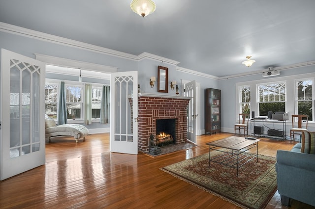 living room with a brick fireplace, french doors, crown molding, and wood finished floors