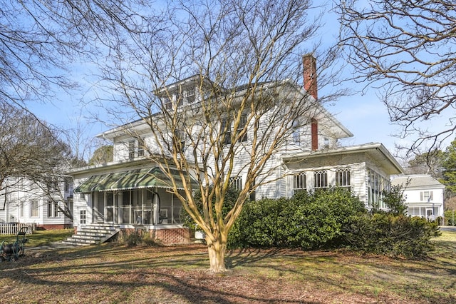 view of front facade featuring a sunroom, a chimney, and a front lawn