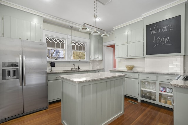 kitchen featuring stainless steel fridge with ice dispenser, a kitchen island, light countertops, pendant lighting, and a sink