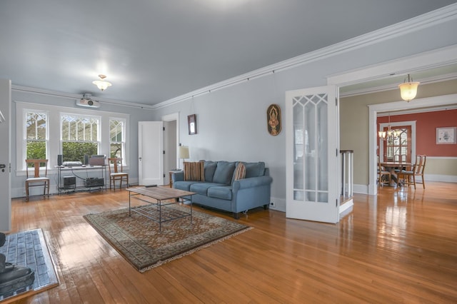 living room featuring a notable chandelier, ornamental molding, wood finished floors, and baseboards