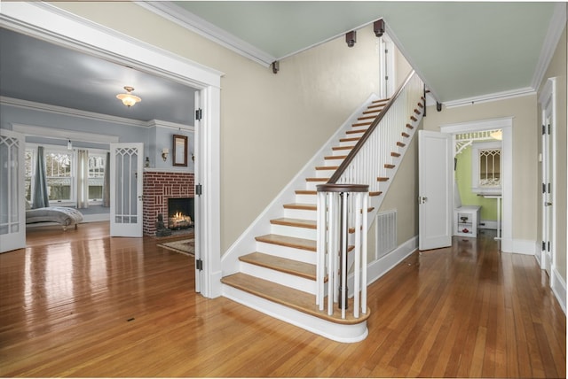 stairway featuring a brick fireplace, visible vents, crown molding, and wood finished floors