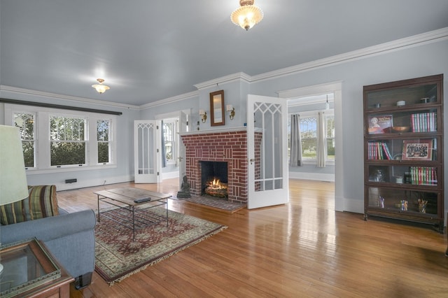 living area with ornamental molding, a fireplace, baseboards, and wood finished floors