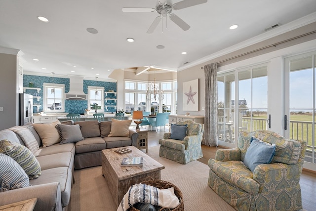 living room with light wood-type flooring, ceiling fan with notable chandelier, and crown molding