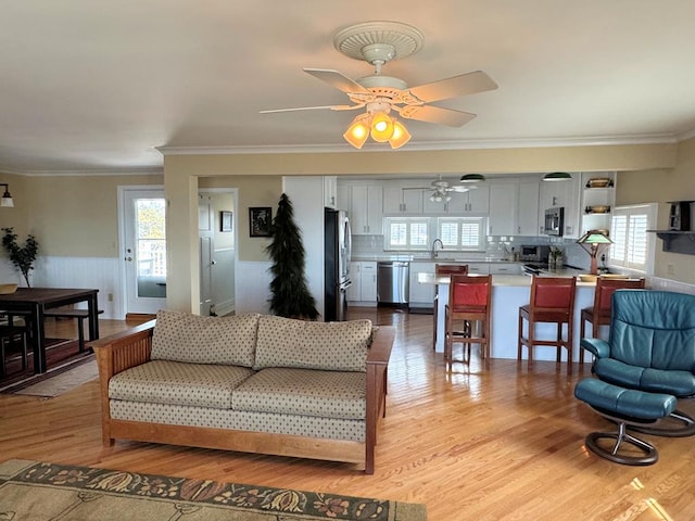 living room featuring ceiling fan, light wood-style flooring, wainscoting, and crown molding