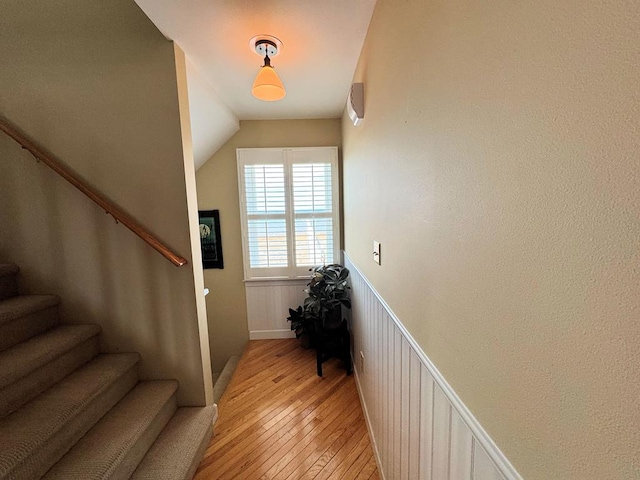 stairs featuring vaulted ceiling, wainscoting, and hardwood / wood-style floors