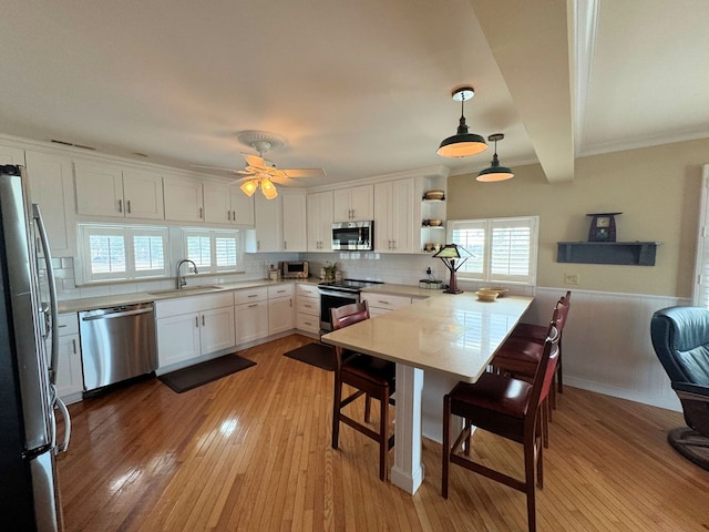 kitchen with a kitchen bar, light wood-type flooring, appliances with stainless steel finishes, a peninsula, and a sink