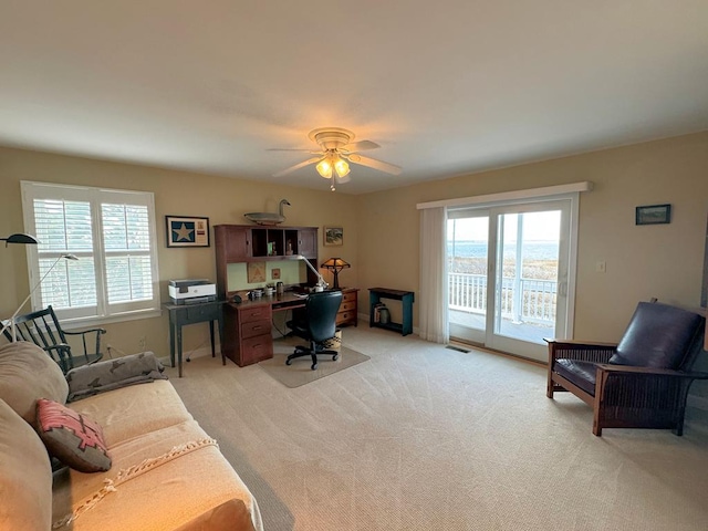 office space with light carpet, visible vents, and ceiling fan