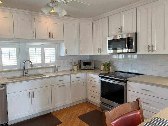 kitchen with tasteful backsplash, light countertops, appliances with stainless steel finishes, white cabinetry, and a sink