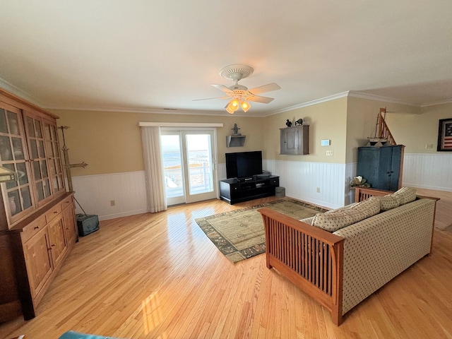 living area with a ceiling fan, light wood-style floors, wainscoting, and crown molding