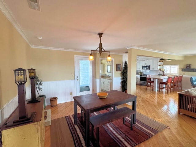 dining room with visible vents, light wood-style flooring, wainscoting, and crown molding