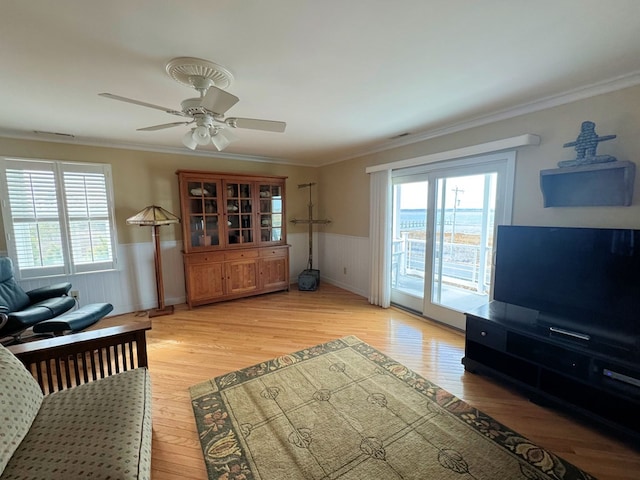 living room with wainscoting, ceiling fan, light wood-style floors, and ornamental molding