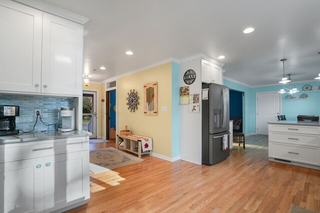 kitchen with backsplash, ornamental molding, white cabinets, stainless steel fridge with ice dispenser, and light hardwood / wood-style floors