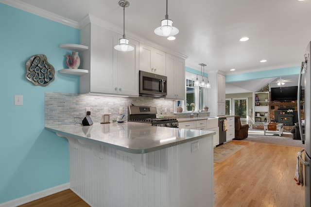 kitchen with backsplash, white cabinets, appliances with stainless steel finishes, decorative light fixtures, and kitchen peninsula