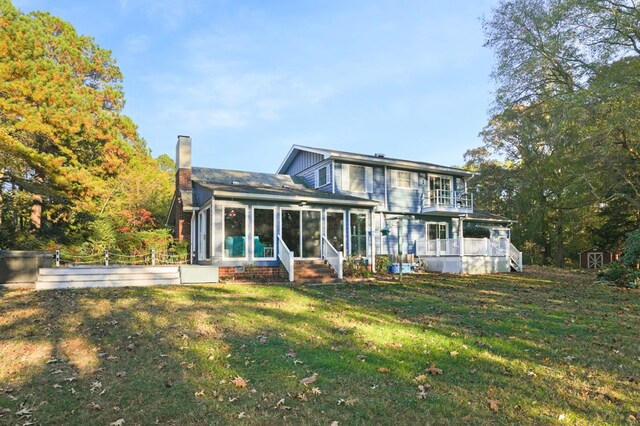 rear view of house with a lawn, a sunroom, a balcony, and a storage shed