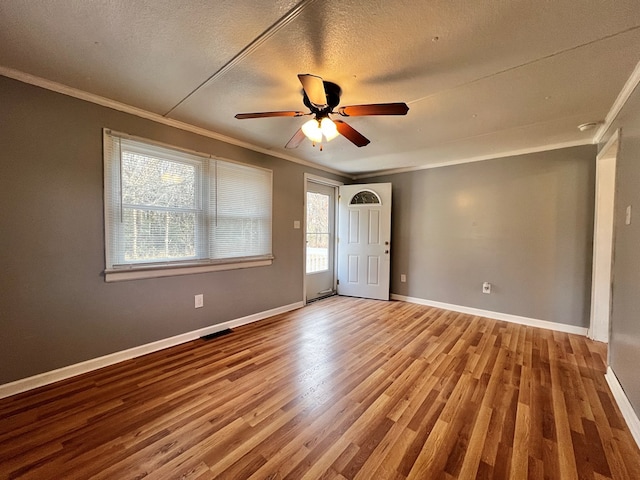 empty room with ceiling fan, ornamental molding, wood-type flooring, and a textured ceiling