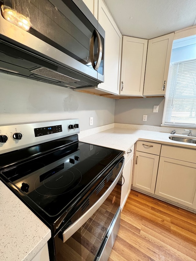 kitchen with appliances with stainless steel finishes, sink, white cabinets, and light wood-type flooring