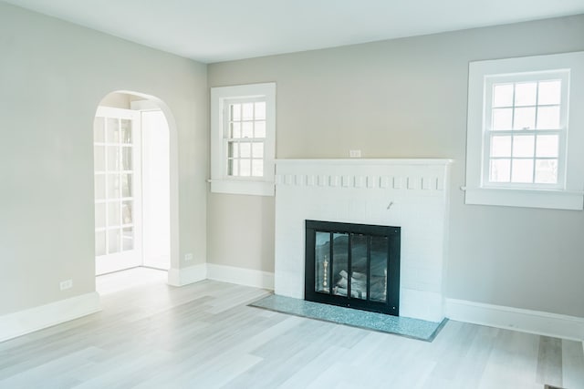 unfurnished living room with a healthy amount of sunlight, light wood-type flooring, and a brick fireplace