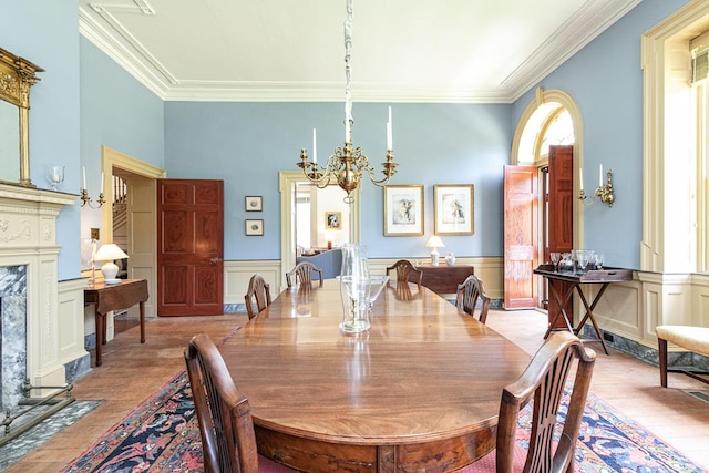 dining area with a high end fireplace, light wood-type flooring, an inviting chandelier, and ornamental molding