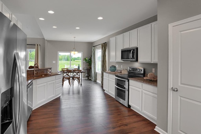 kitchen with white cabinets, sink, hanging light fixtures, dark stone countertops, and appliances with stainless steel finishes