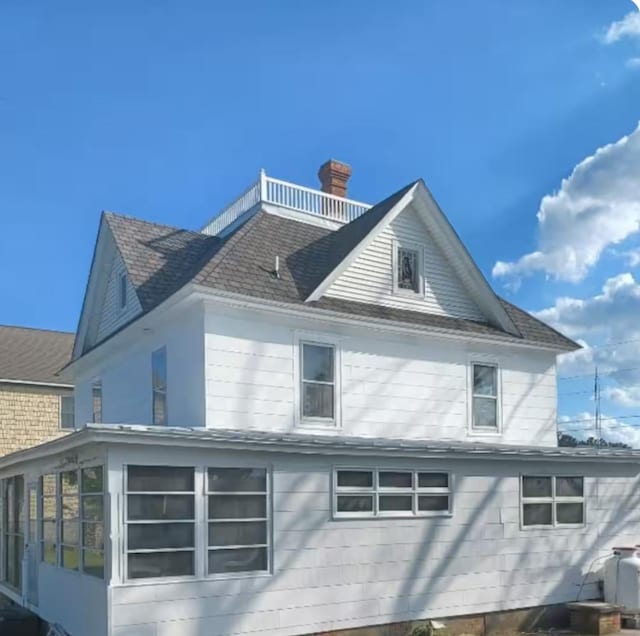 view of side of home with roof with shingles, a chimney, and a sunroom