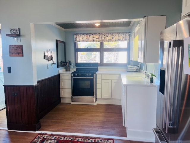 kitchen featuring a wainscoted wall, a sink, white cabinetry, range with gas cooktop, and stainless steel fridge with ice dispenser