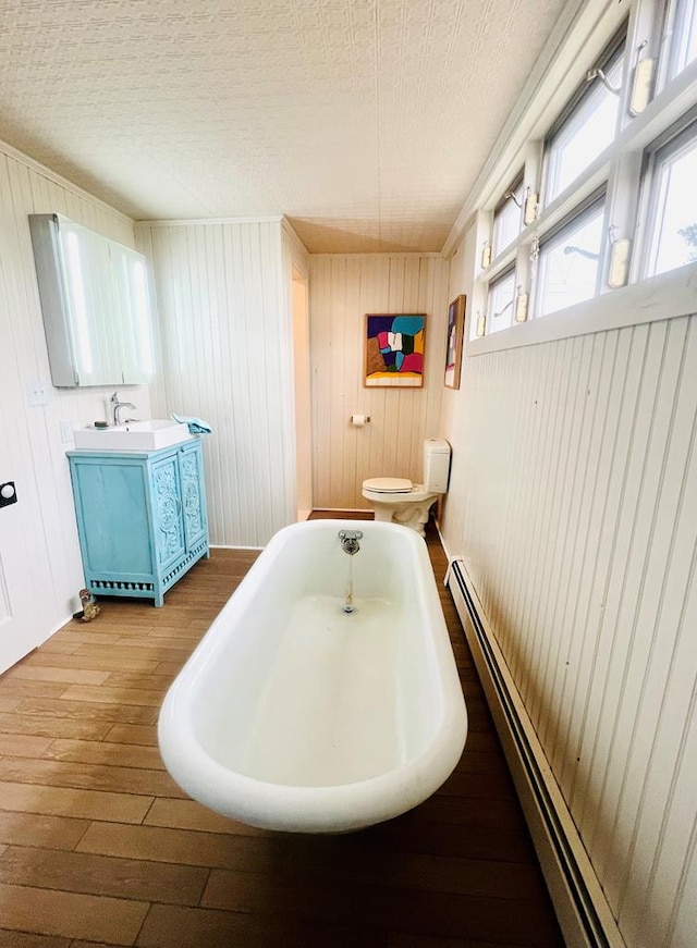 bathroom featuring toilet, a tub to relax in, a baseboard heating unit, wood finished floors, and vanity