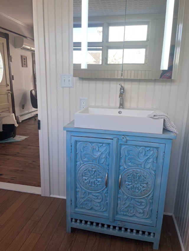 room details with a baseboard heating unit, wood finished floors, vanity, and a wall mounted AC