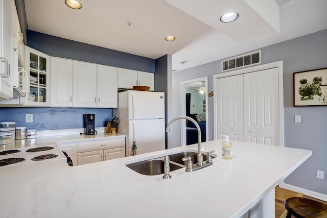 kitchen with electric stove, sink, white cabinetry, a kitchen breakfast bar, and white fridge