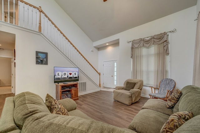 living room with visible vents, stairs, wood finished floors, baseboards, and a high ceiling