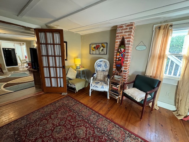 living area featuring beamed ceiling, a healthy amount of sunlight, and hardwood / wood-style flooring