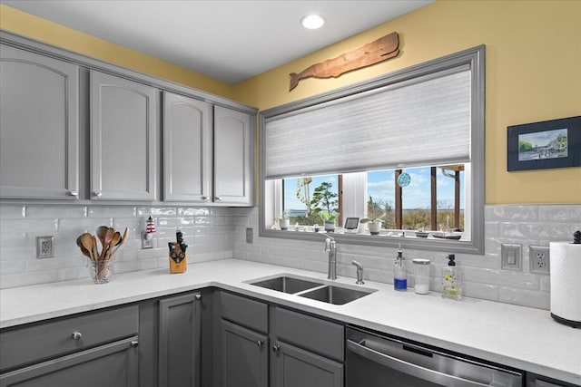 kitchen featuring gray cabinetry, a sink, light countertops, dishwasher, and backsplash