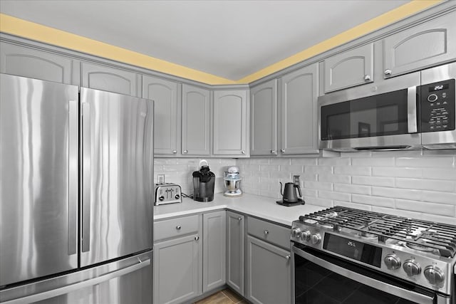 kitchen featuring gray cabinetry, light countertops, light tile patterned floors, decorative backsplash, and appliances with stainless steel finishes