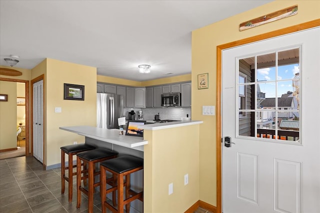 kitchen with a breakfast bar area, a peninsula, gray cabinets, appliances with stainless steel finishes, and tasteful backsplash