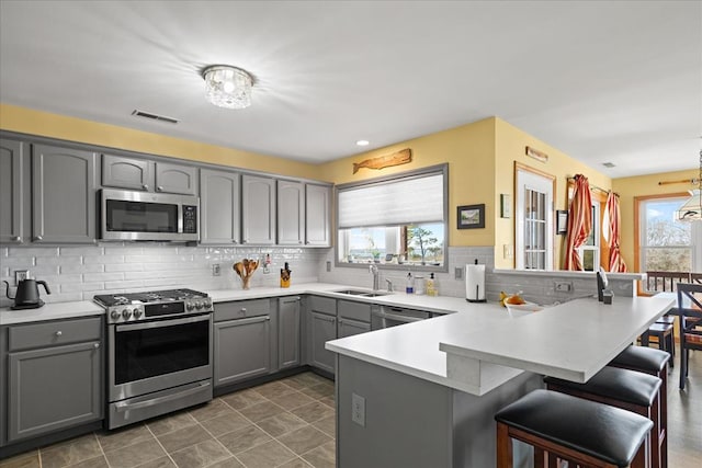 kitchen with visible vents, a peninsula, gray cabinets, a sink, and stainless steel appliances