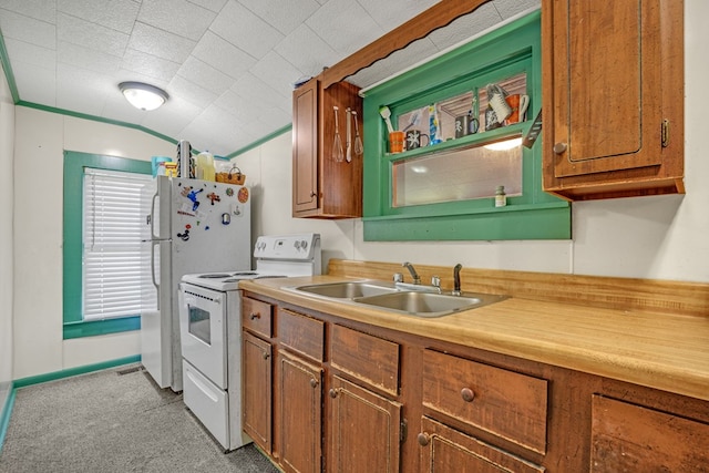kitchen with a sink, brown cabinets, white appliances, light countertops, and light colored carpet