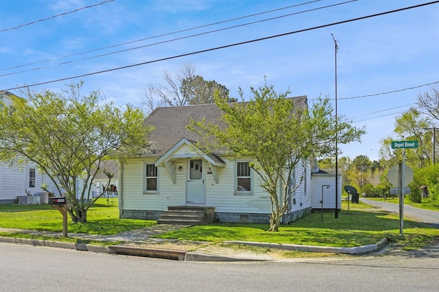 view of front of home featuring central AC, a shingled roof, and a front yard