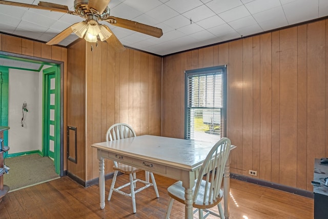 dining space featuring baseboards, wooden walls, wood finished floors, and a ceiling fan