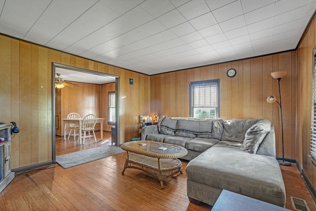 living area with visible vents, hardwood / wood-style flooring, wood walls, and a ceiling fan