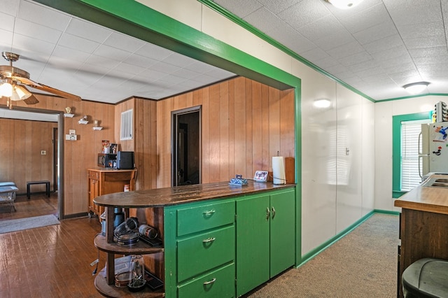 kitchen featuring a ceiling fan, ornamental molding, wooden walls, green cabinetry, and freestanding refrigerator