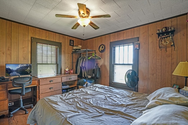 bedroom featuring crown molding, wood finished floors, wood walls, and ceiling fan