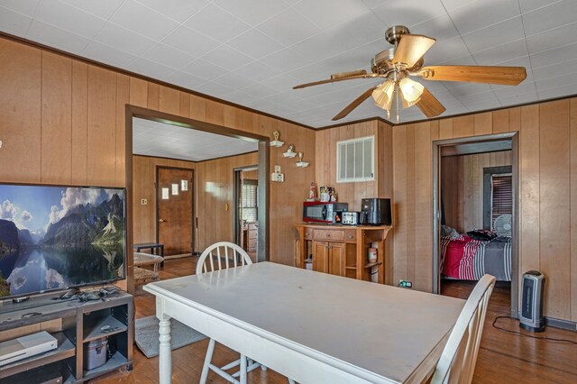 dining space with wood finished floors, wooden walls, visible vents, and ceiling fan