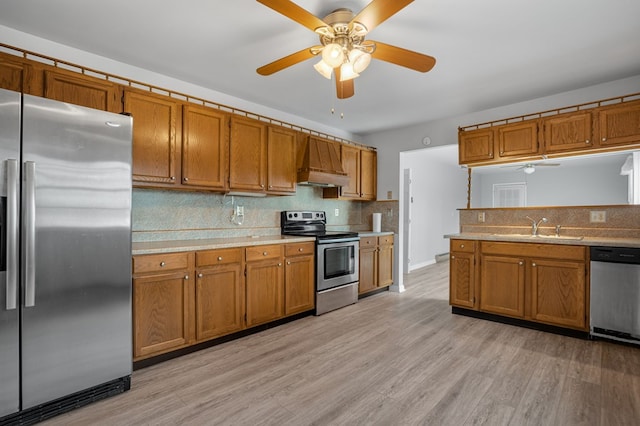 kitchen featuring sink, appliances with stainless steel finishes, custom range hood, decorative backsplash, and light wood-type flooring