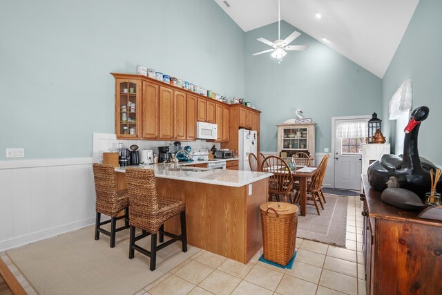 kitchen with a kitchen bar, white appliances, kitchen peninsula, and high vaulted ceiling