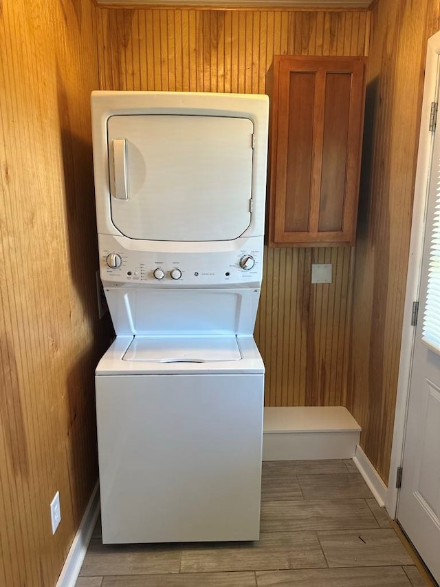clothes washing area with laundry area, wood walls, stacked washer / dryer, and wood finished floors