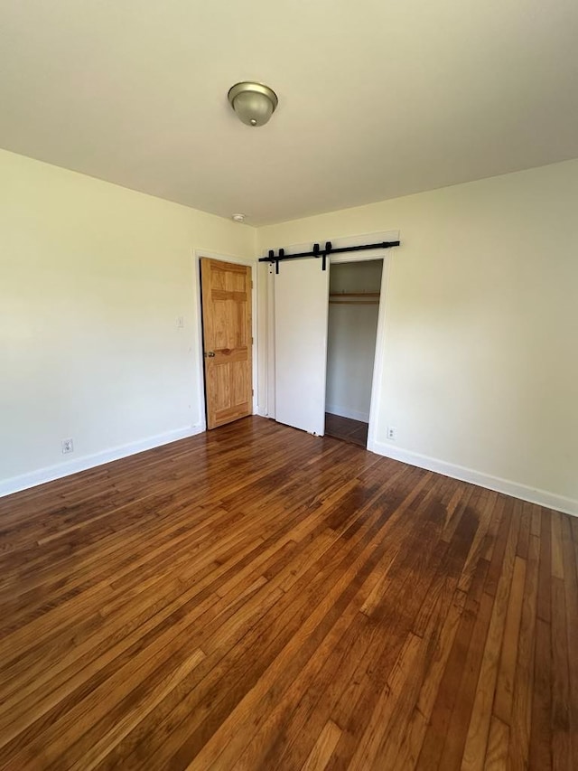 unfurnished bedroom featuring baseboards, a barn door, dark wood finished floors, and a closet