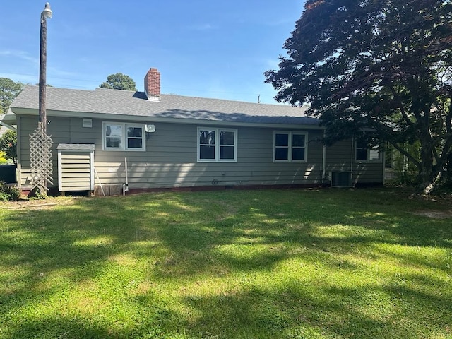 back of property featuring a lawn, central AC unit, a chimney, and roof with shingles