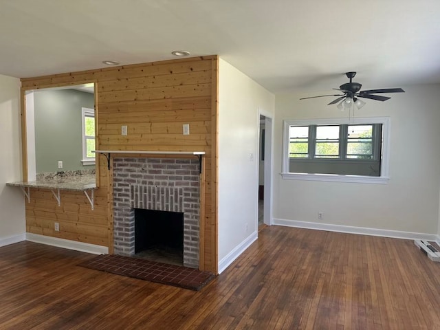 unfurnished living room with baseboards, ceiling fan, a brick fireplace, and dark wood-style flooring