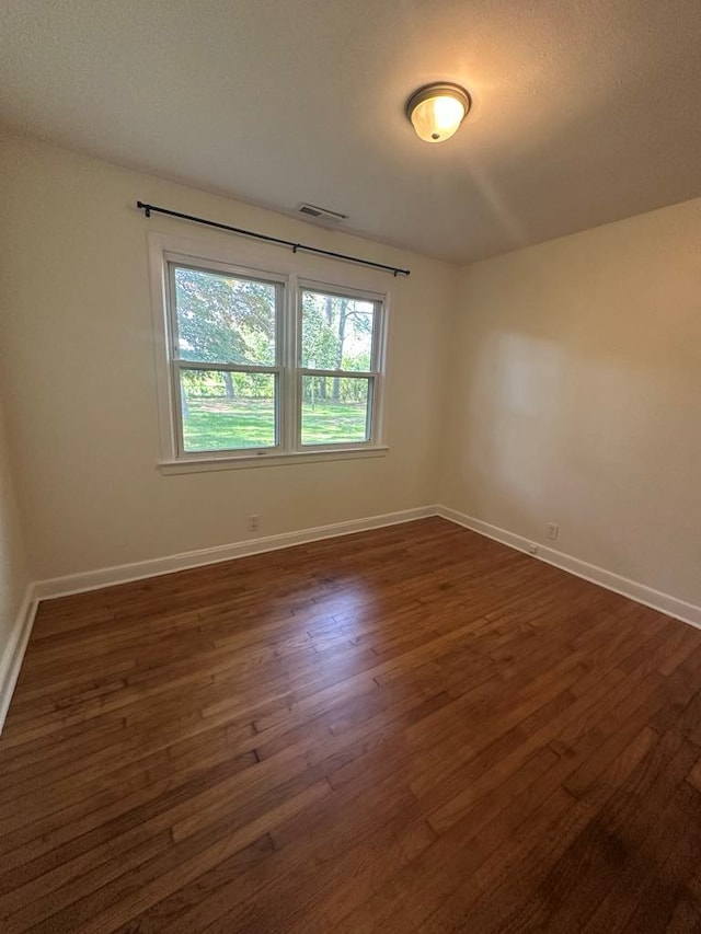 unfurnished room featuring baseboards, dark wood-style flooring, and visible vents