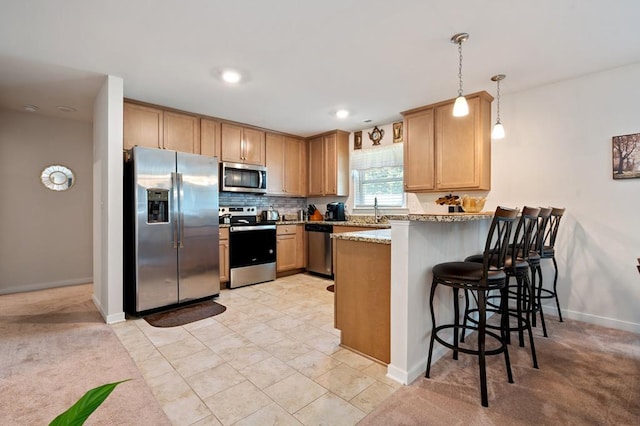 kitchen with a kitchen bar, appliances with stainless steel finishes, kitchen peninsula, light stone counters, and pendant lighting