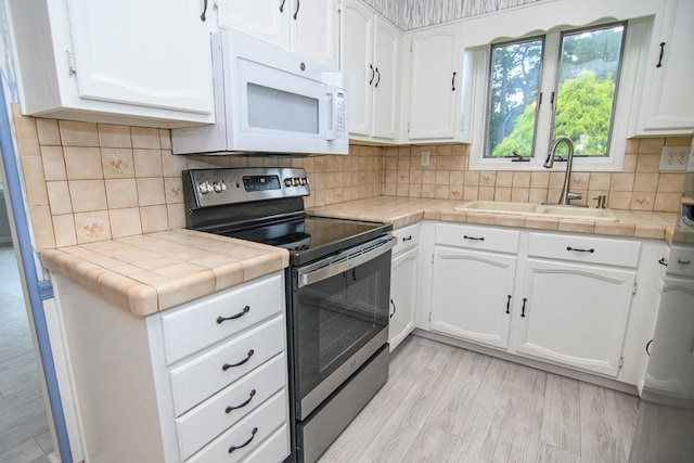 kitchen with electric stove, sink, and white cabinets